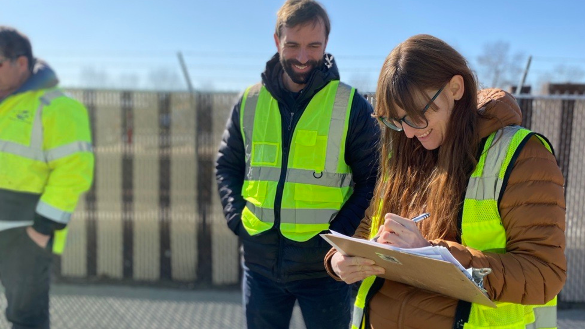 Two people in high visibility vests with a clipboard smiling