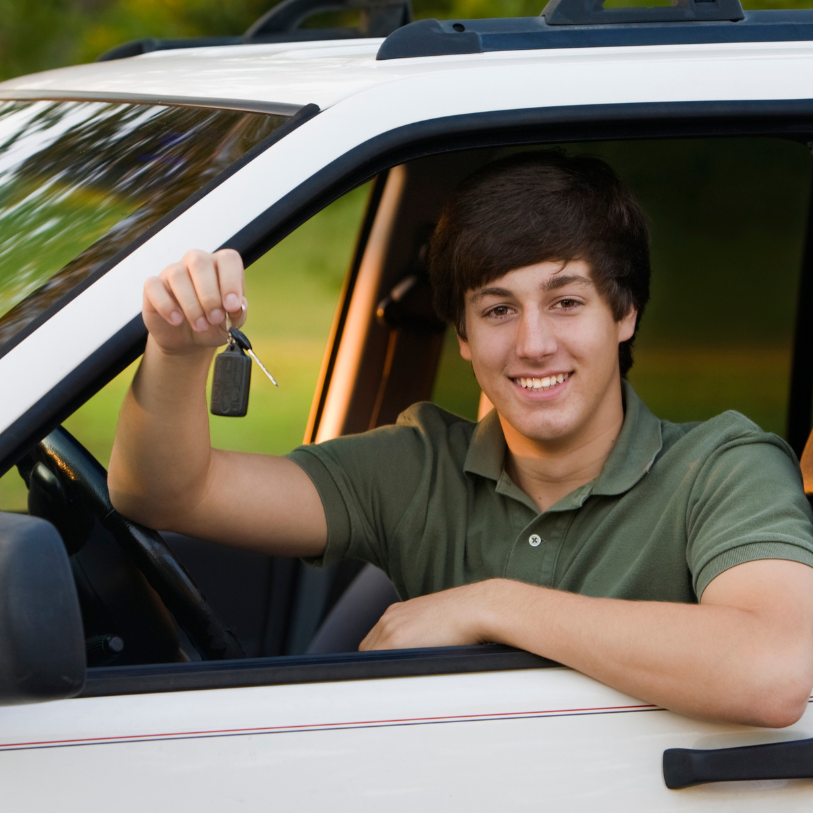 Teenage male holds keys out the window of a white car while smiling.